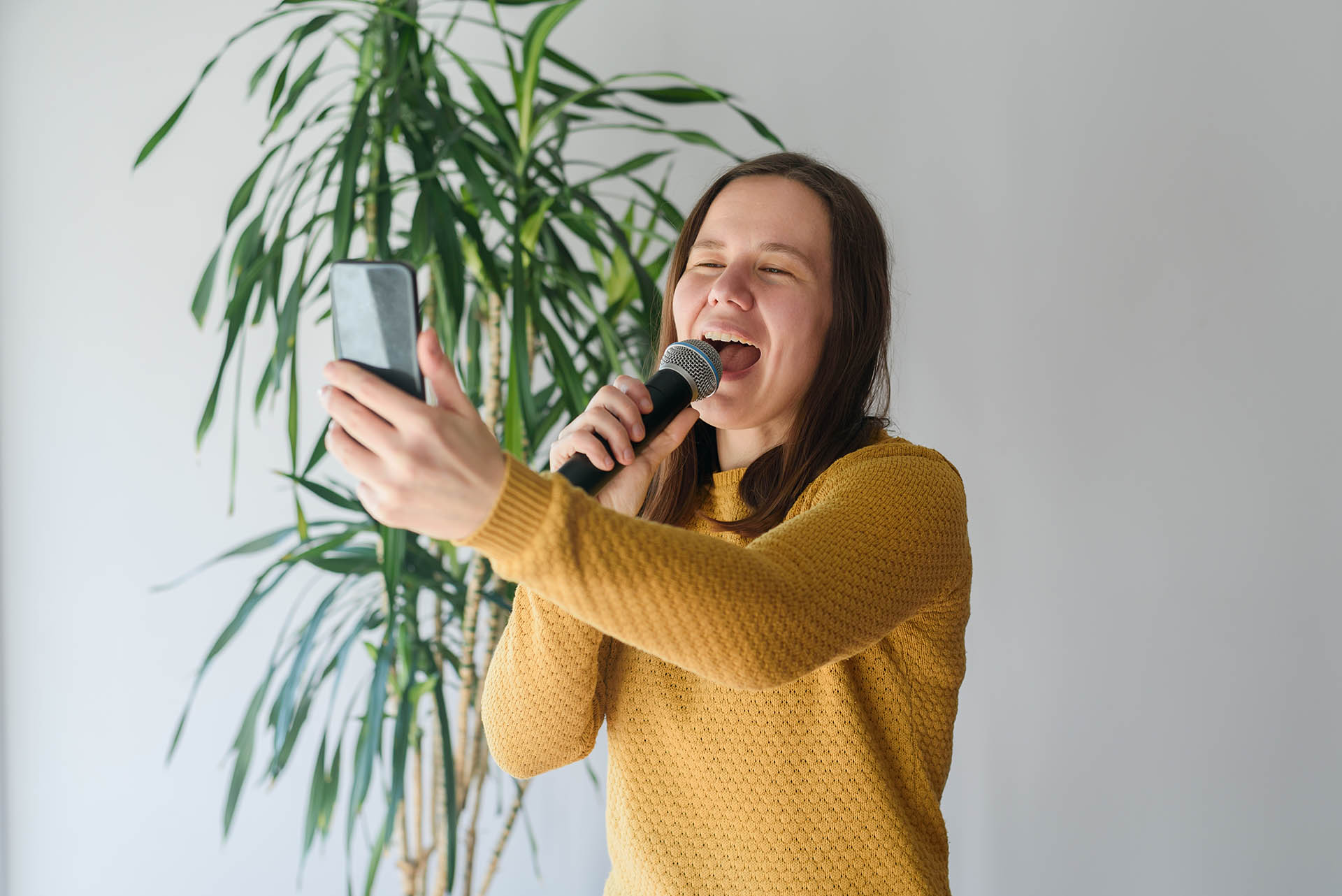 Woman blogger singing with microphone at home with expression. Taking selfie or video stream